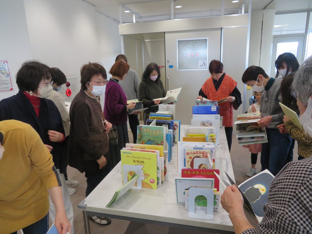 人々がテーブルの周りで本を手に取りながら話し合っている様子の画像。