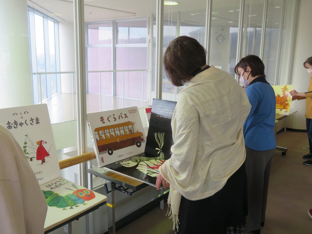 展示会で作品を見ている数人の人々とその前に置かれた展示物が写っている画像。