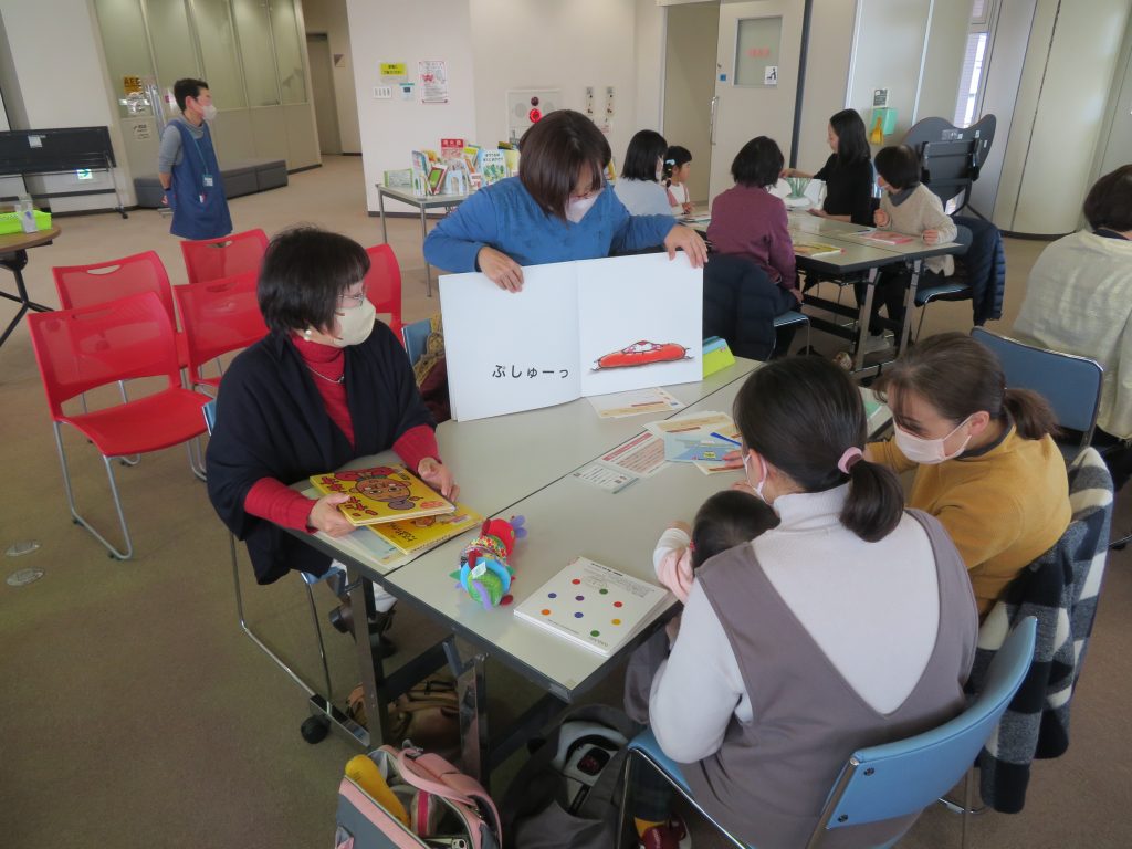 子どもたちと大人がテーブルを囲んで活動している様子で、掲示板に絵が描かれている。