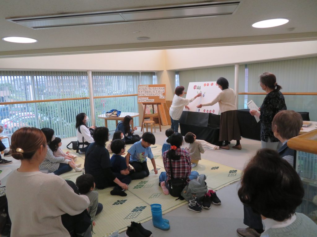 教室で子供たちが座っている中、大人がホワイトボードに何かを示している様子。