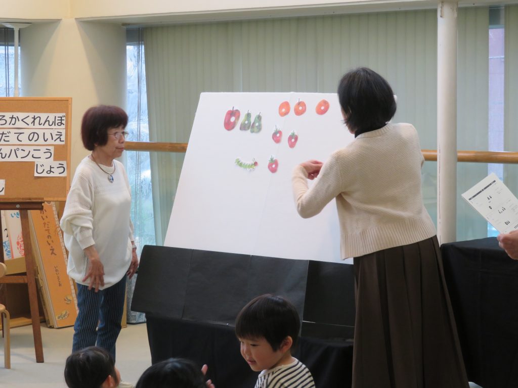 子供たちが見守る中、女性がボードに絵を描いている様子。