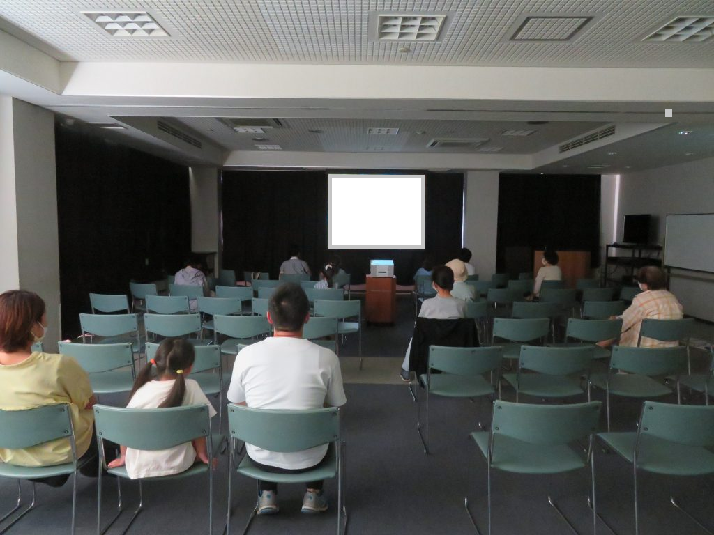 会議室でプレゼンテーションを受ける参加者たちの様子。