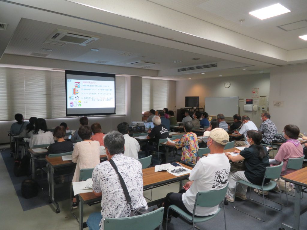 教室でプレゼンテーションを受ける多くの人々が座っている様子。