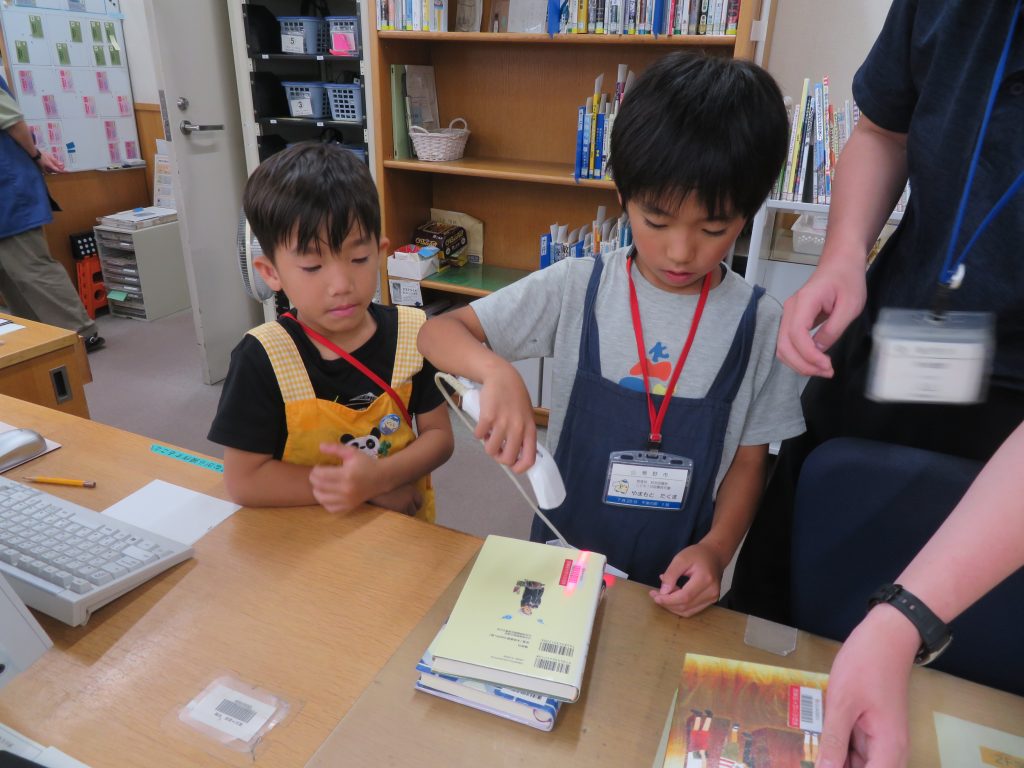 子どもたちが図書館のカウンターで本を扱っている様子。