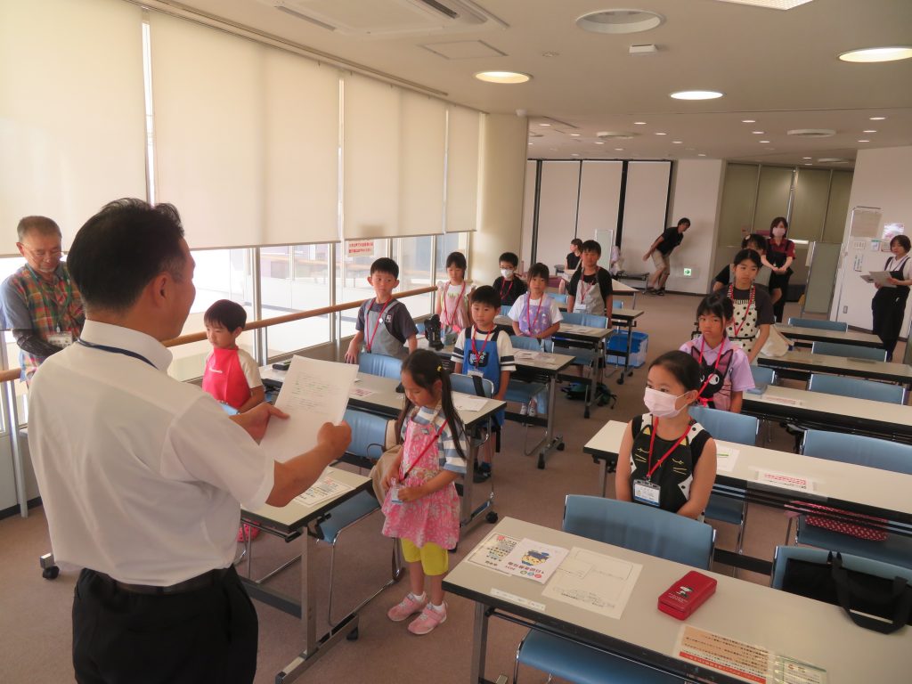 教室で子どもたちが座り、先生が何かを説明している様子。