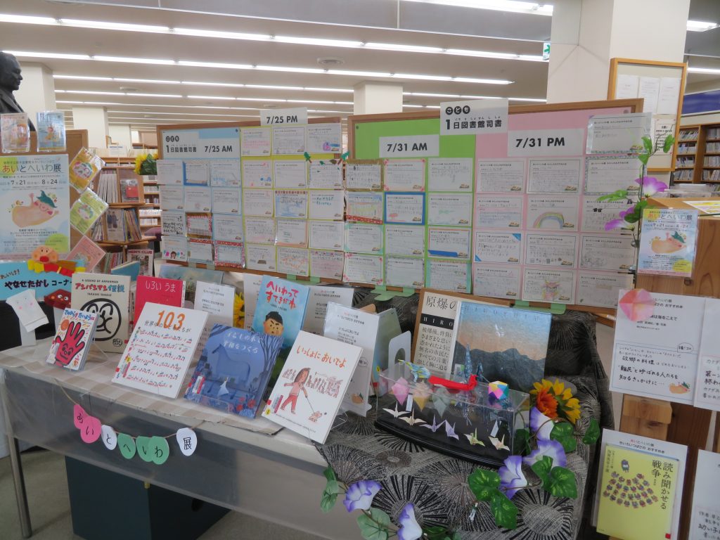 書籍やカードが並ぶ棚とその上に掲示されたスケジュールボードが映っている画像。