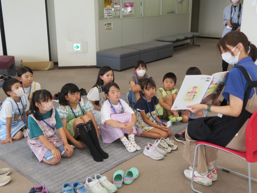 子どもたちが座っている前で大人が絵本を読んでいる場面。