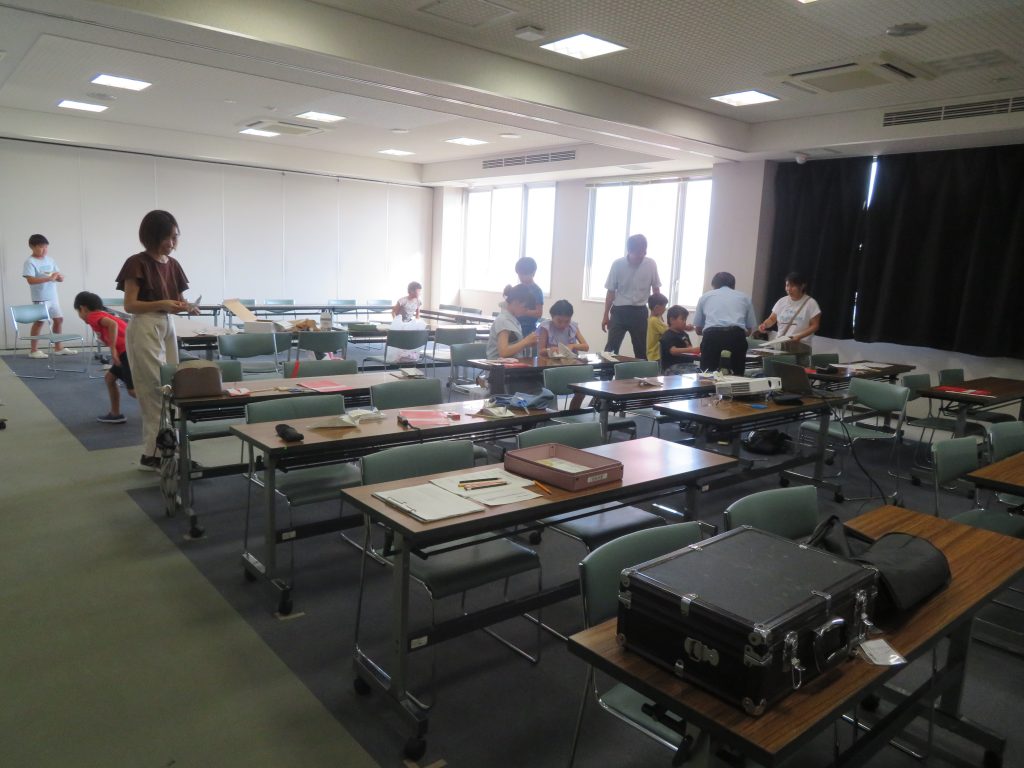教室の中で複数の人々が机の周りで活動している様子。
