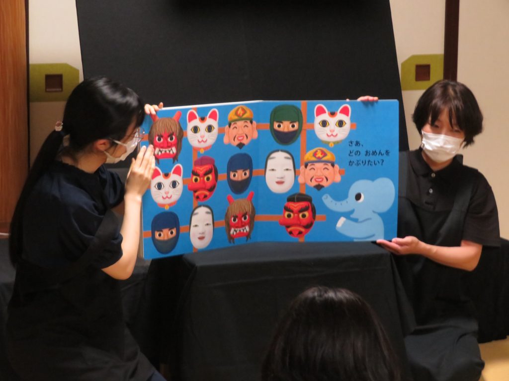 二人の女性がカラフルなキャラクターが描かれたボードを指差している様子。