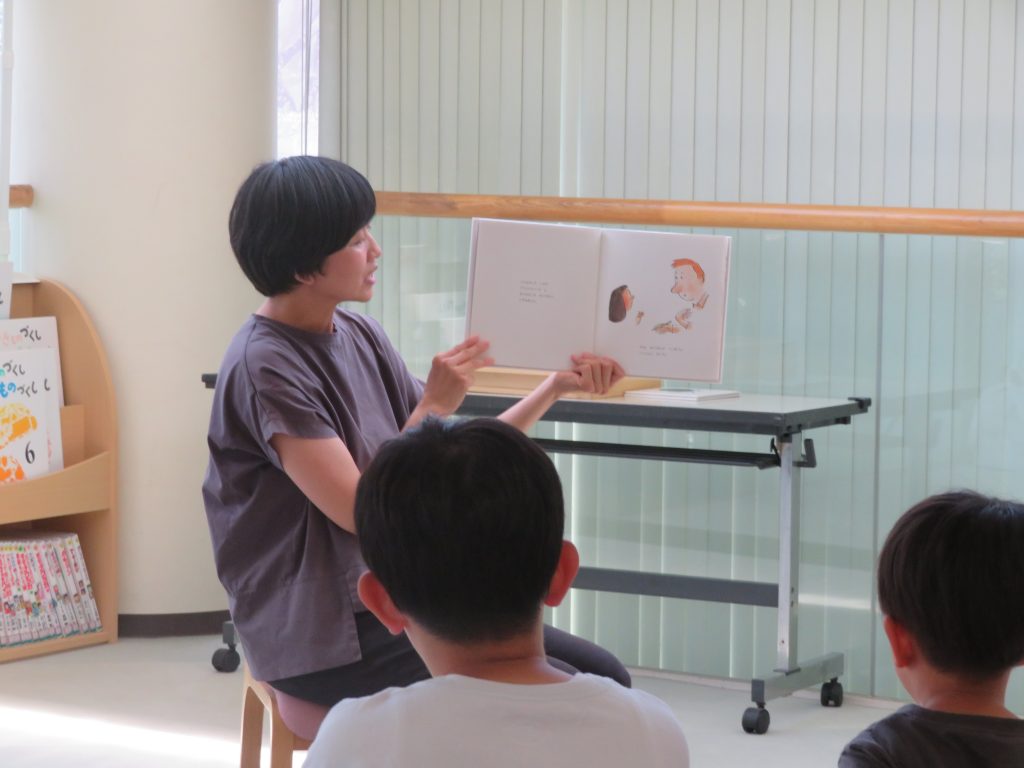 子供に絵本を読んでいる人が椅子に座っている様子。