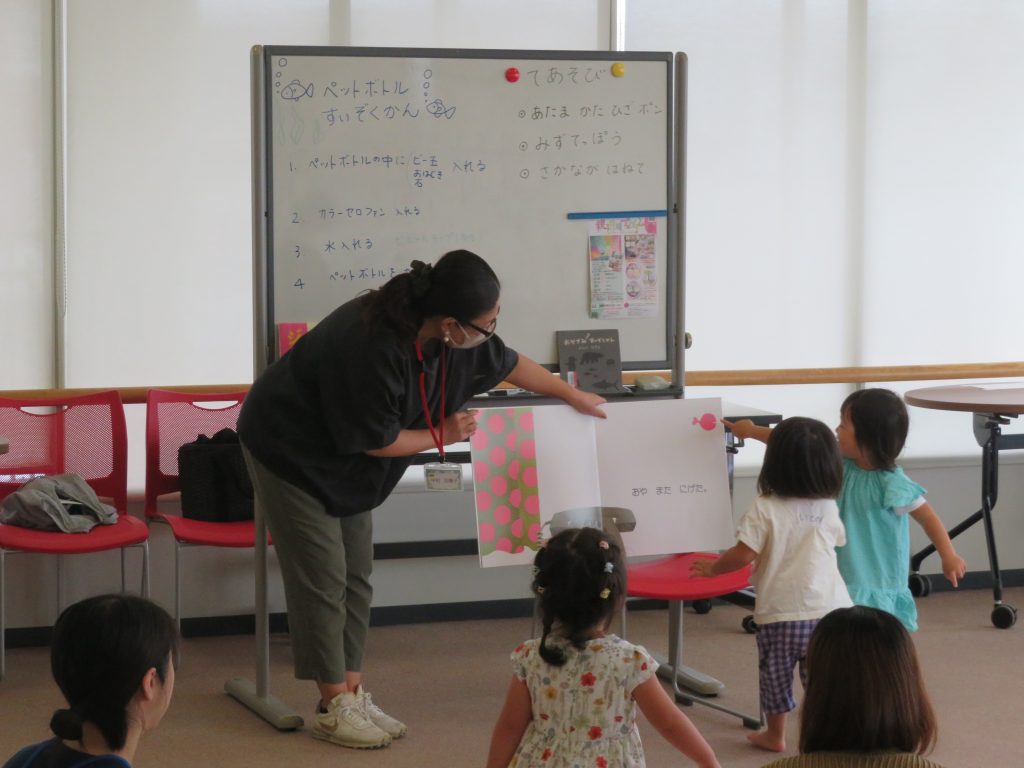 教室で子供たちに何かを教えている大人とその周りの子供たちの様子。