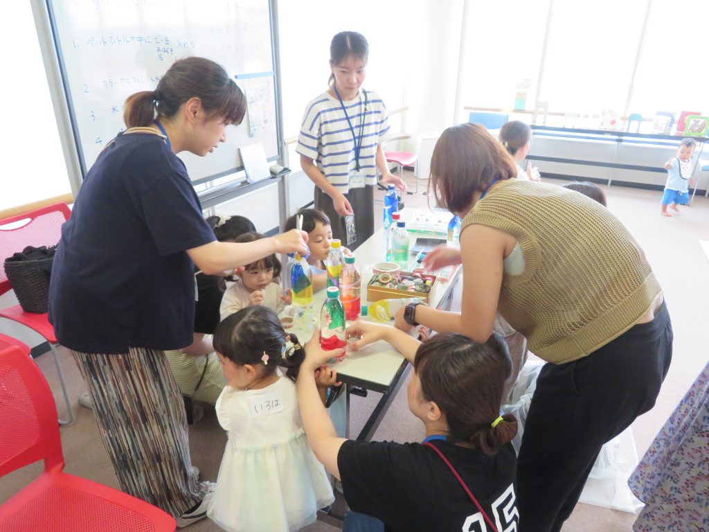 子供たちと大人がテーブルで何かを作ったり遊んだりしている様子の写真。