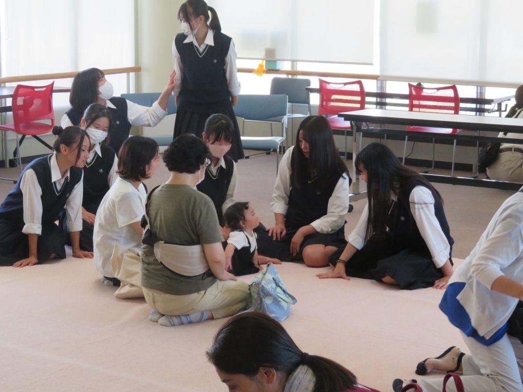 複数の人々が床に座り、子供と交流している様子の写真です。