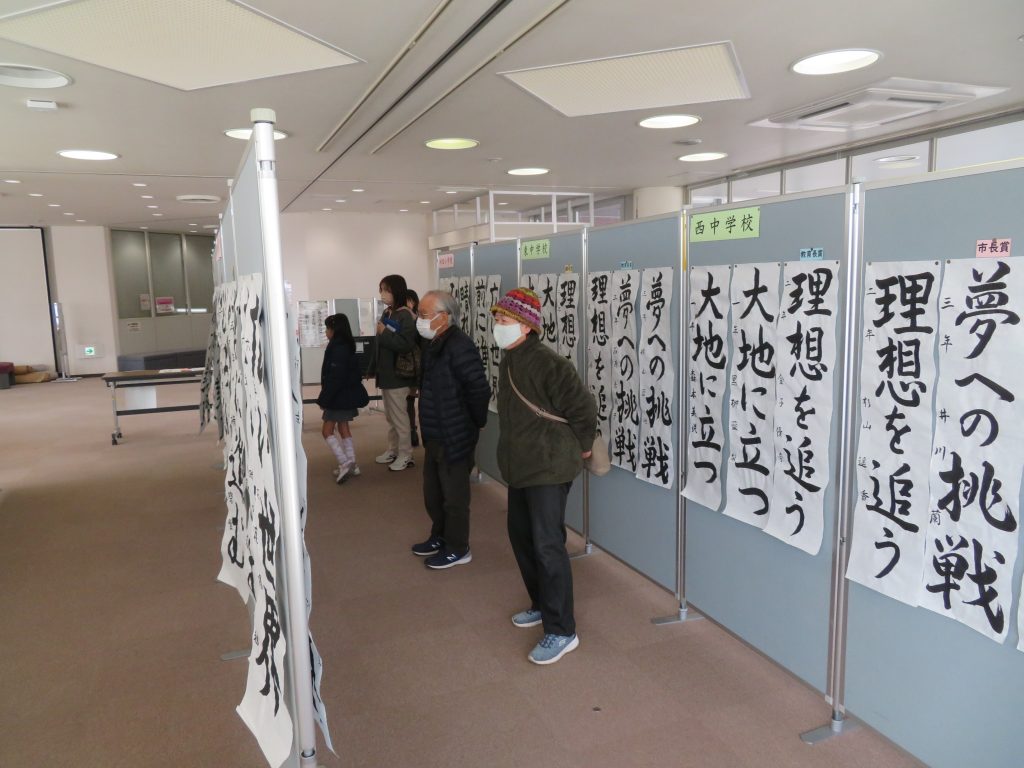 書道作品が展示されている室内で数人が作品を見ている様子。